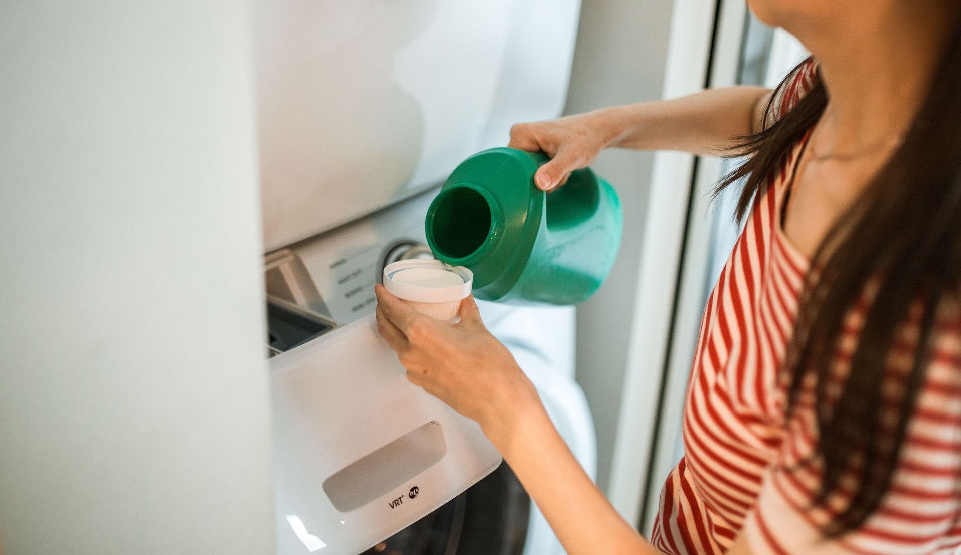A woman pours detergent into a washing machine in a home laundry room.