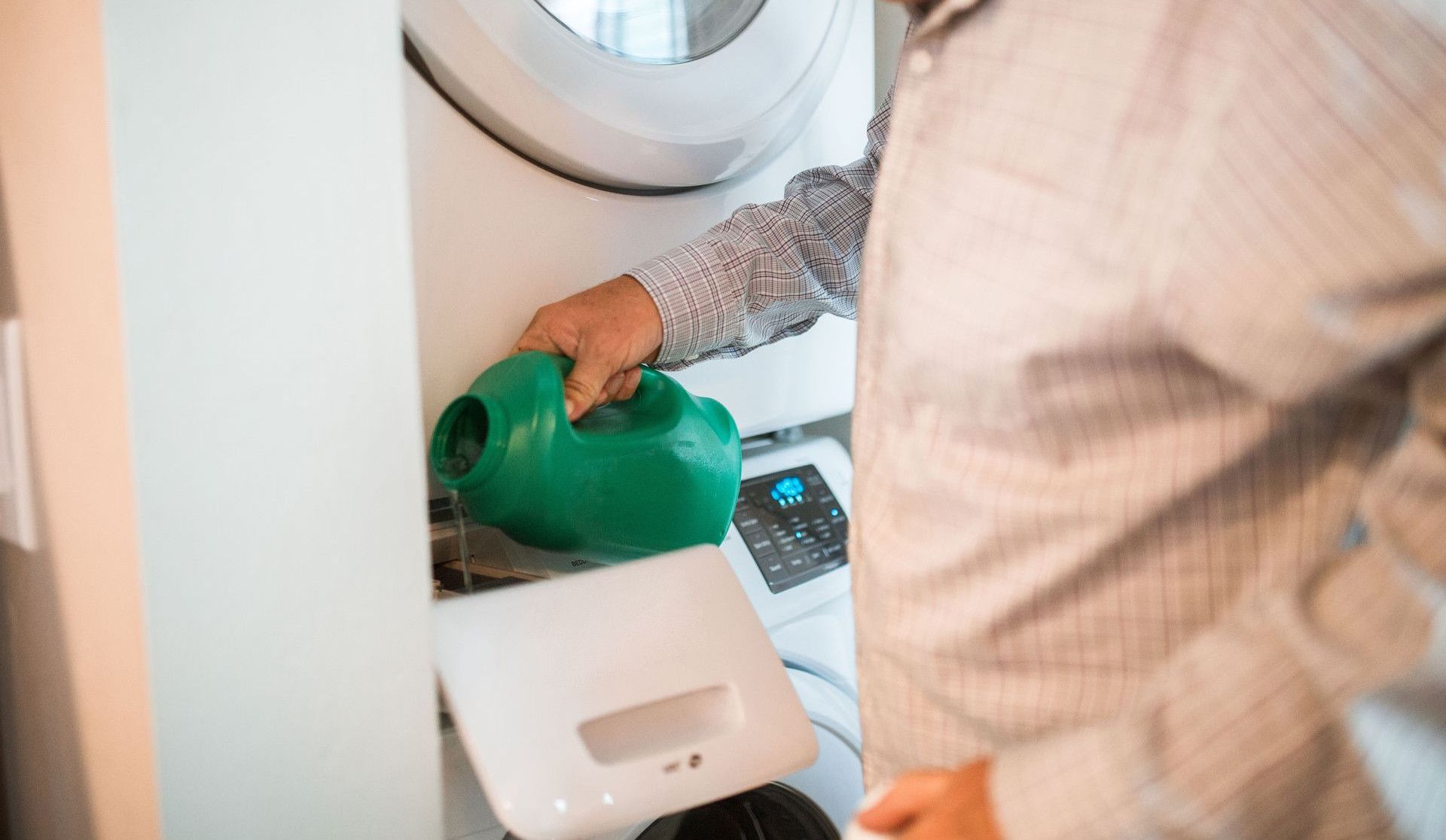 An adult man pours detergent into a washing machine for doing laundry indoors.